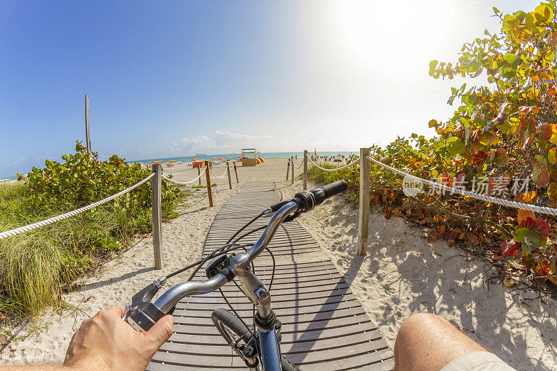 视角拍摄的一个年轻的运动男子骑自行车到海滩南海滩，迈阿密海滩，迈阿密，南佛罗里达，美国