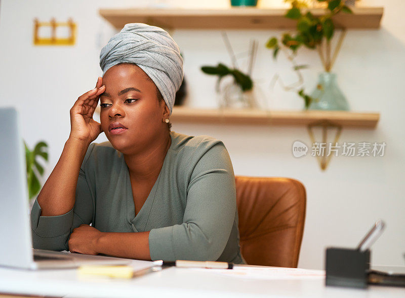 非裔美国女商人坐在办公室看着她的笔记本电脑屏幕，看起来有压力或感到泄气。女性企业家在做项目时感到疲惫和缺乏灵感