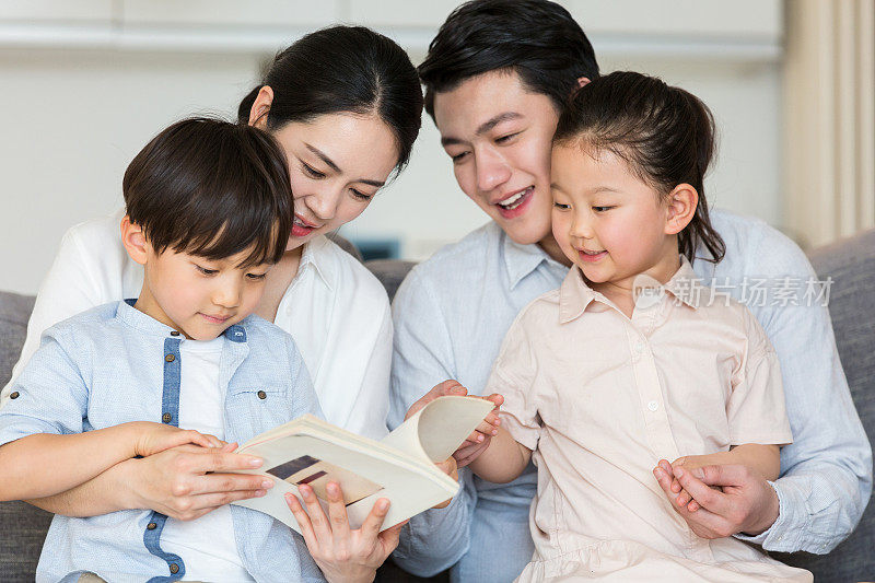 一对父母和他们的两个儿子和女儿一起读儿童故事书-图片