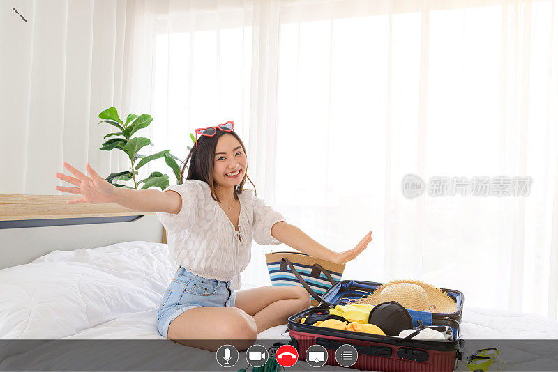 年轻的亚洲女性博主微笑着在夏天的休闲服装交谈facetime视频打电话关于夏天的旅行与智能手机在卧室。使用视频聊天在线应用与麦克风，视频，电话，共享屏幕，直接消息图标，社交距离，概念