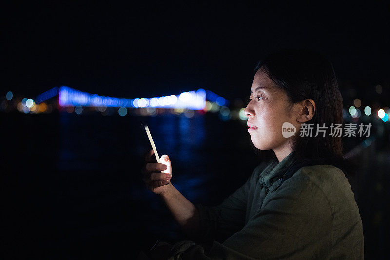 年轻女性游客晚上在城市里使用智能手机