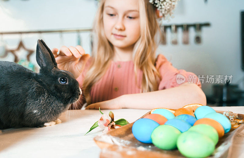 美丽的女孩头戴花圈庆祝复活节。烹饪蛋糕，在厨房桌子上画鸡蛋。节日快乐在一起。和复活节兔子玩，兔子
