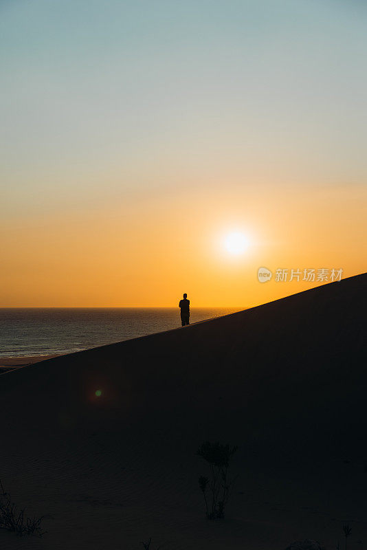 一个男人旅行者的剪影，在土耳其海边的沙丘上凝视着风景优美的日落