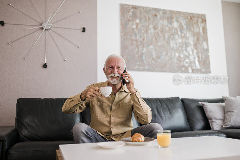 微笑的老人一边吃早餐一边用他的智能手机