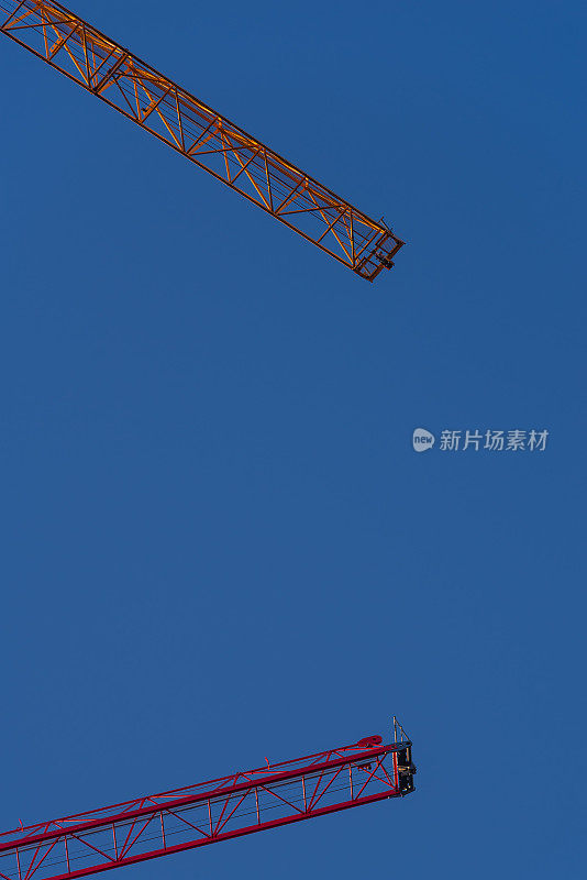 两架红色建筑起重机在蓝天的映衬下垂直低角度拍摄