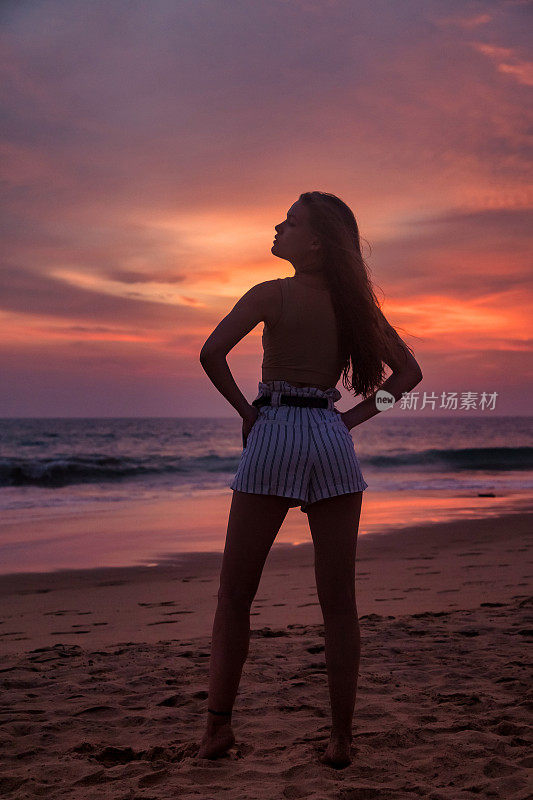 背影的剪影年轻女子站在沙滩上在海上日落的背景，夏天。在热带海岸享受轻松愉快的假期。旅游度假度假概念。复制广告文字空间