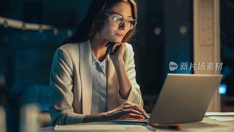 特写一个年轻的会计在办公室工作到深夜。积极女性使用笔记本电脑，为财务总监准备工作分配和公司报告。