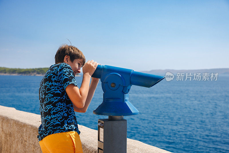 夏日里，一个男孩从小镇的海滨用双筒望远镜眺望