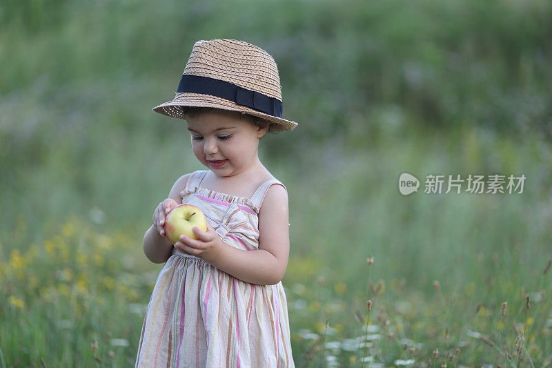 可爱的小女孩在户外吃苹果的照片