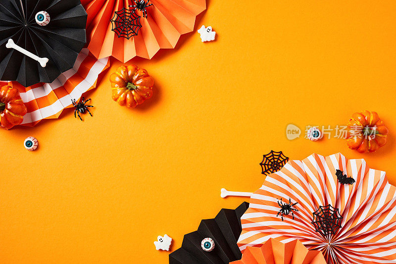 万圣节快乐的节日概念。平铺构图用万圣节的装饰品，折叠纸扇，南瓜，骨头，血色的眼睛，蜘蛛网，幽灵在橙色的背景。