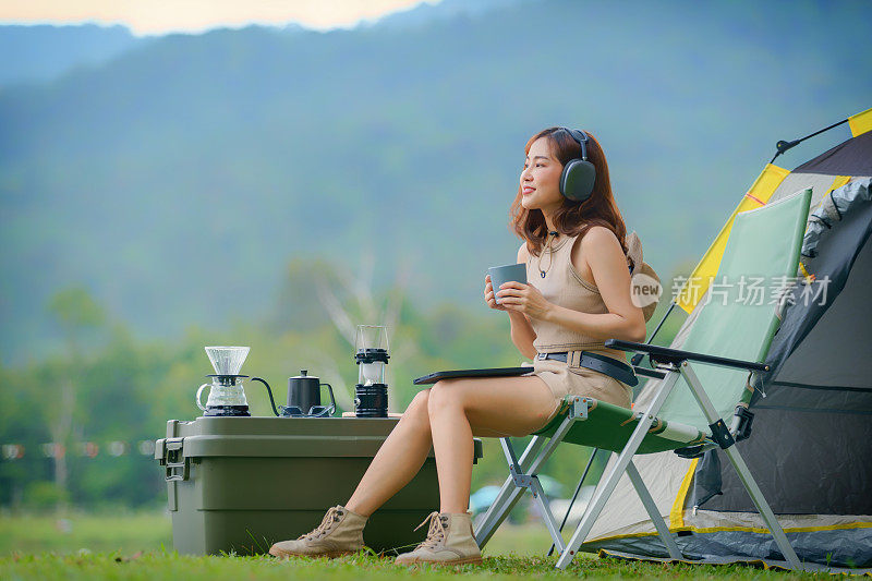 时髦的亚洲女性露营者戴着耳机，独自享受音乐露营。