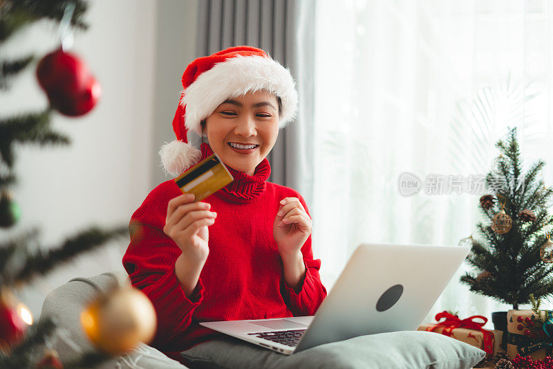 亚洲妇女开心地微笑着用笔记本电脑和信用卡买圣诞礼物。