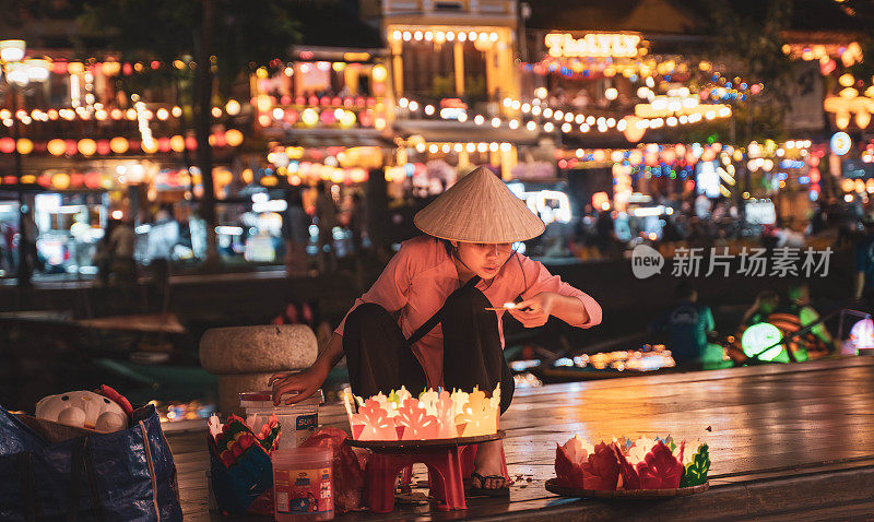 年轻的越南妇女在会安夜市出售传统的蜡烛和灯笼。