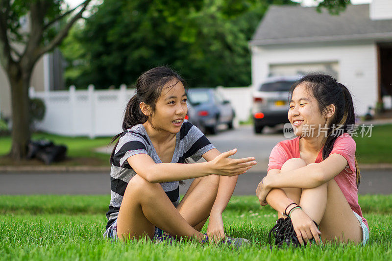 两个亚洲女孩坐在前门的草坪上