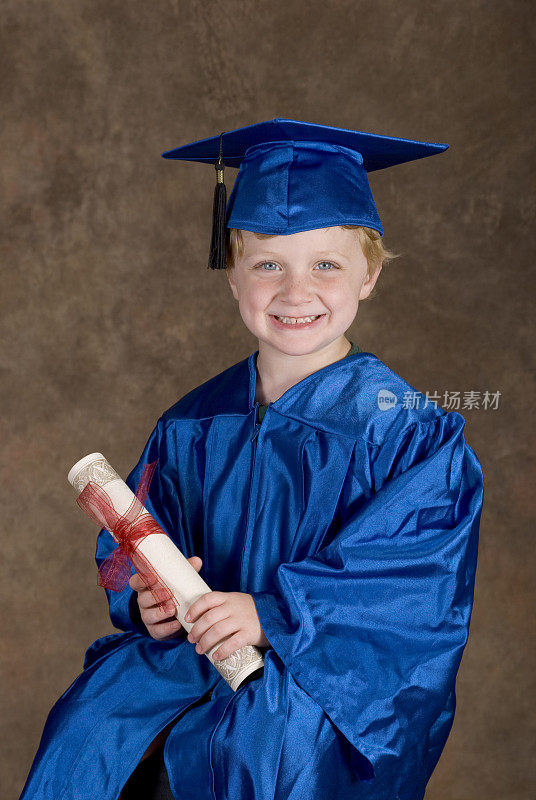 幼儿园毕业照，可爱的小男孩拿着毕业证书，毕业礼服和学位帽