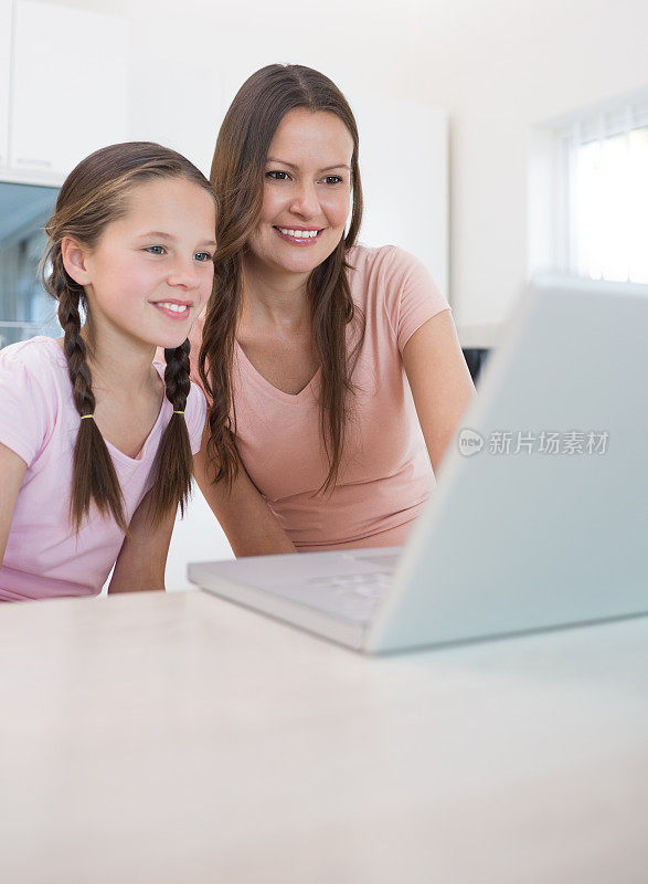 母亲和小女儿在厨房使用笔记本电脑