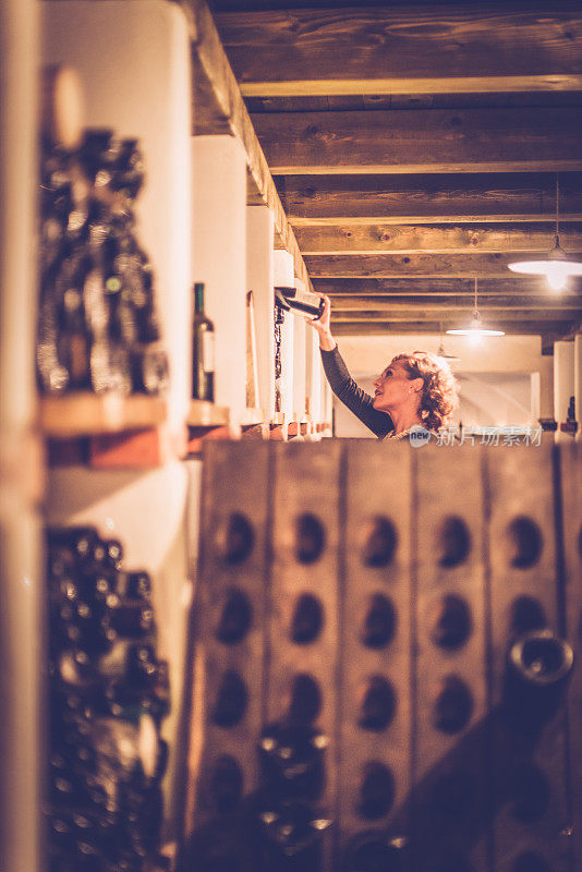 满意的女酿酒师检查酒瓶，酒窖在欧洲