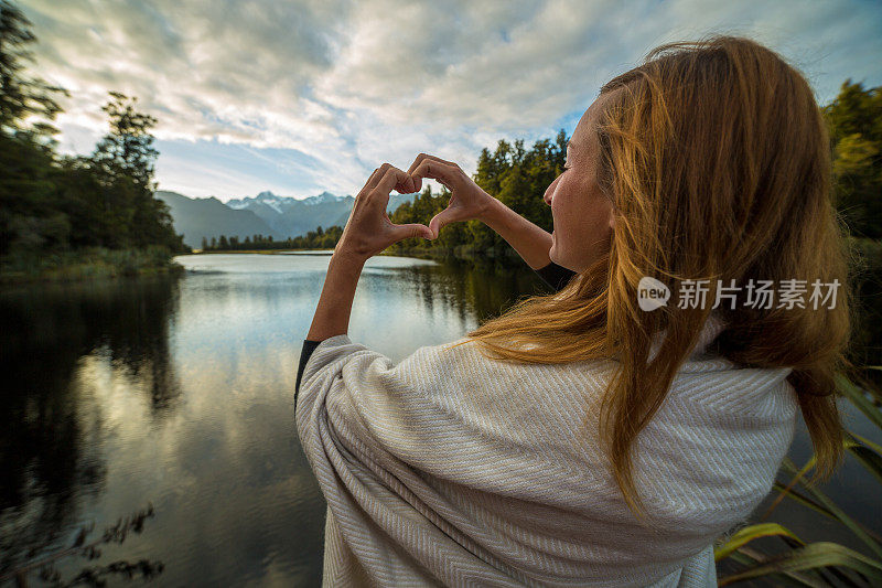 女人在山湖景观上做心形指架