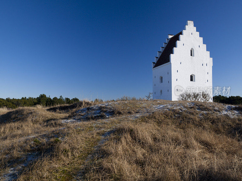 在晴朗的天空下，沙子掩埋了丹麦斯卡根的白色教堂