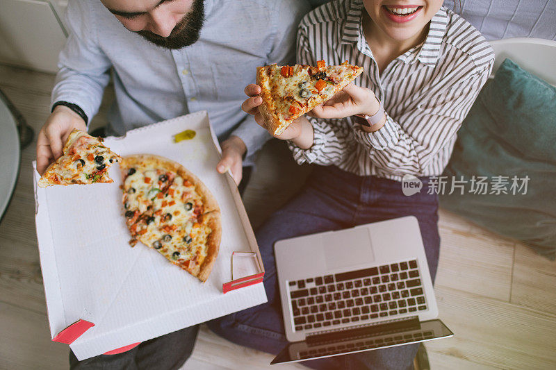 年轻的潮男女夫妇在家用笔记本电脑吃披萨