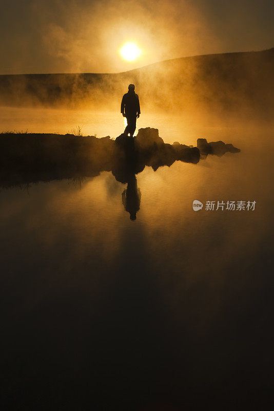 早晨的阳光和雾环绕剪影远足者在平静的湖