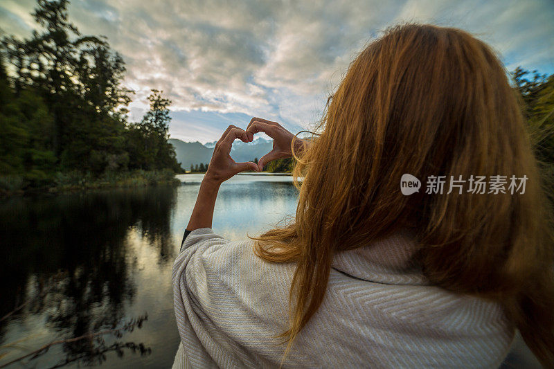 女性在山湖景观上做心形指架