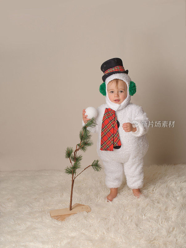 站在雪人服装的婴儿在光秃秃的圣诞树