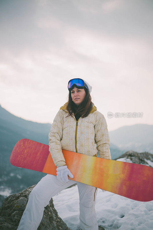 女人拿着滑雪板，背景是高山