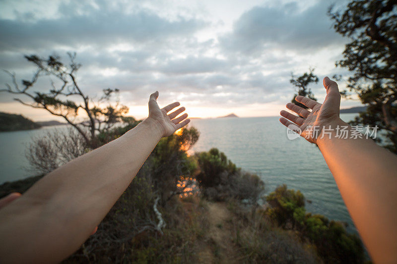 在新西兰豪拉基湾，一个女人的手臂伸向夕阳