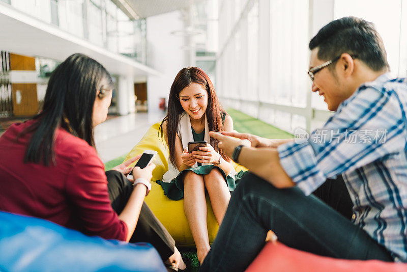 三个亚洲大学生或同事一起使用智能手机。有趣的现代生活方式，社交网络，或通讯技术小玩意的概念，注重中间女孩，景深效果