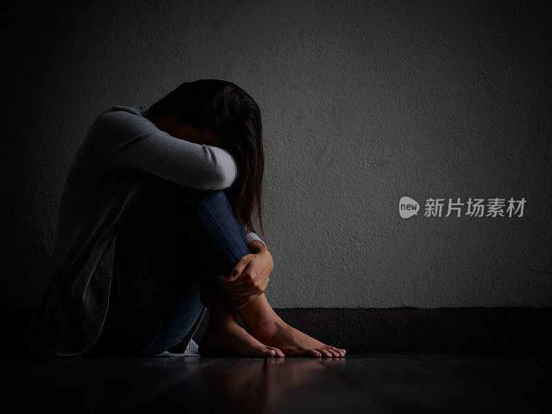 悲伤的女人抱着膝盖哭泣。一个悲伤的女人独自坐在空荡荡的房间里。