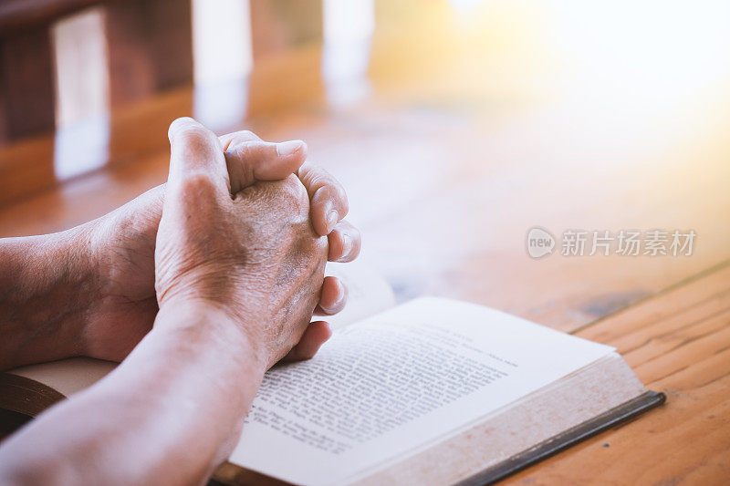 老妇人双手合十，在圣经上祈祷