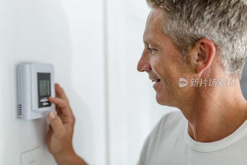 微笑的男人在调节家庭供暖系统的温控器