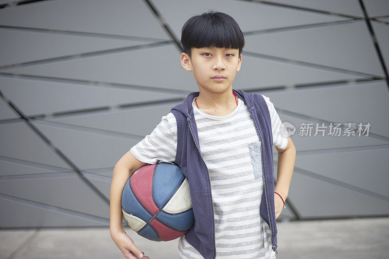 酷酷的亚洲孩子在户外拿着篮球的肖像