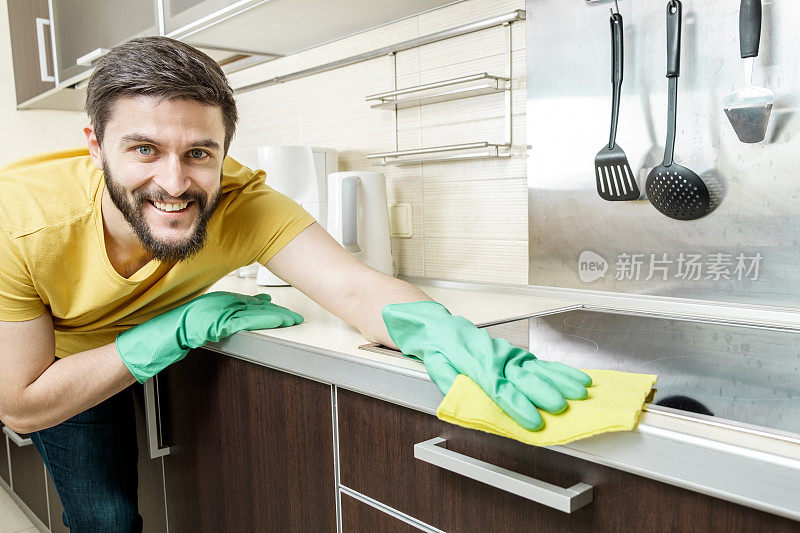 戴着绿色防护手套的年轻人正在用黄色抹布清洁现代厨房