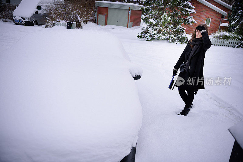 冬天即将来临。女人在冰冷的天气里，车被雪覆盖着。