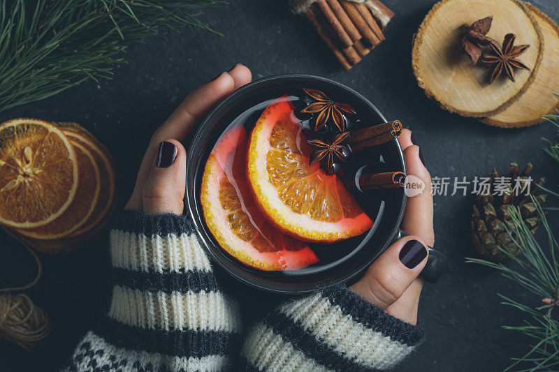 俯视图的女孩的手在一个冬天的毛衣是拿着一个大的黑色杯热热的热葡萄酒。舒适的冬季假期的概念。