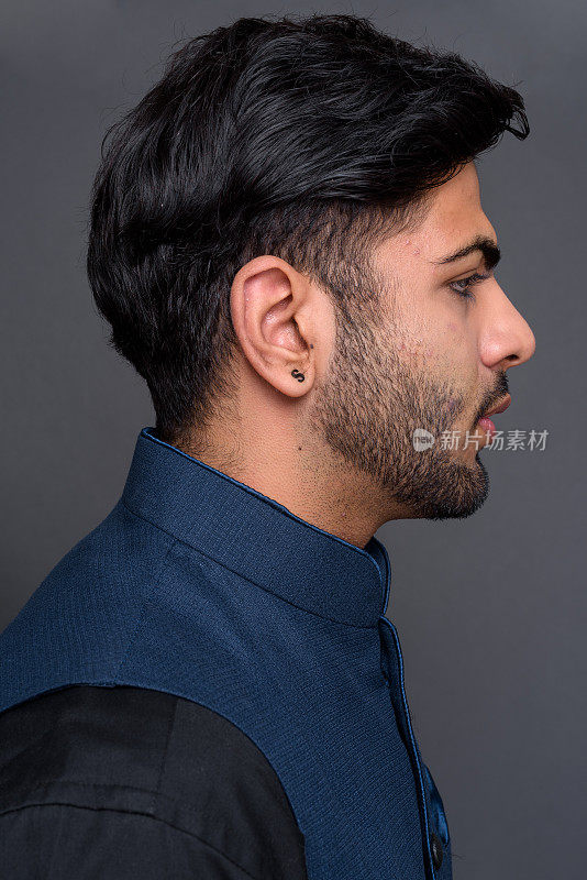 年轻的留胡子的英俊的印度男子穿着传统服装，以灰色的背景