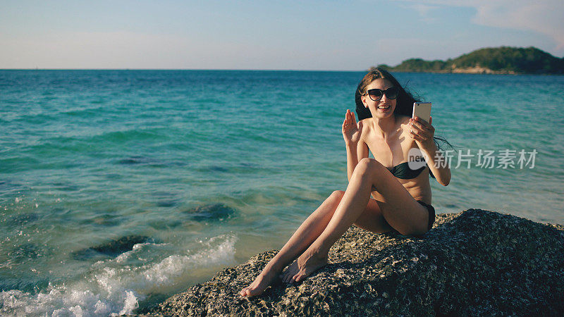 年轻快乐的女人与朋友通过互联网使用智能手机在海洋海滩聊天