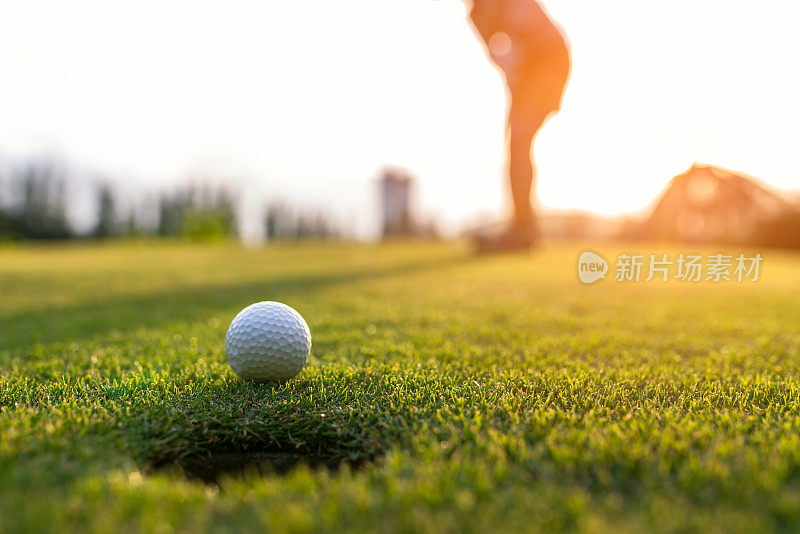 高尔夫球手亚洲女人把高尔夫球在绿色高尔夫在太阳日落傍晚时间，选择焦点。健康和生活方式的概念。