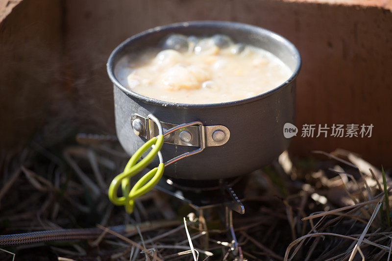 一个特写，一个沸腾的锅在燃气primus为徒步旅行者做饭。