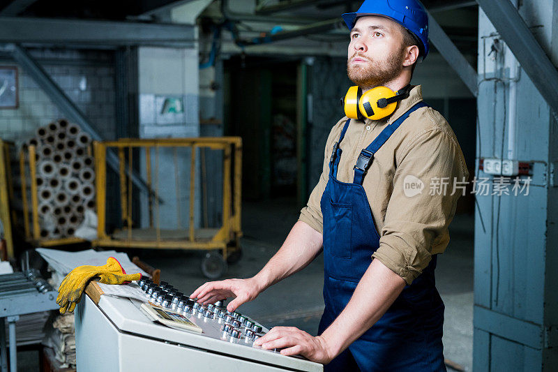 年轻英俊的大胡子工人聚精会神地站在控制板上操作着工业机器，他骄傲地抬起头来