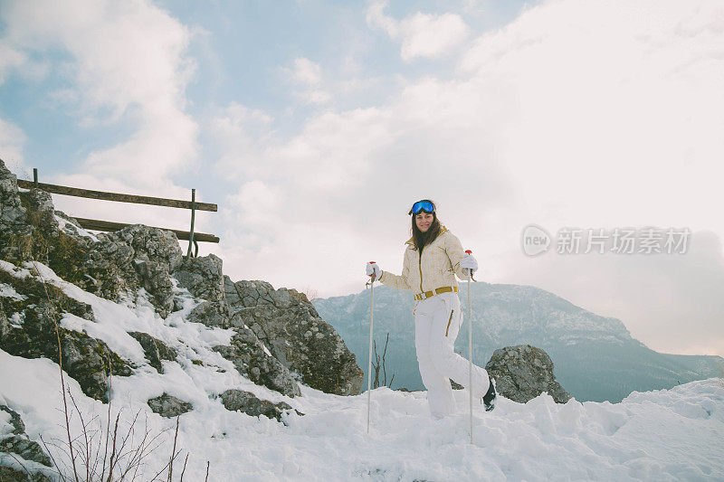 近景美丽的年轻女子在冬天的衣服站在一边，手拿木棍的背景雪山