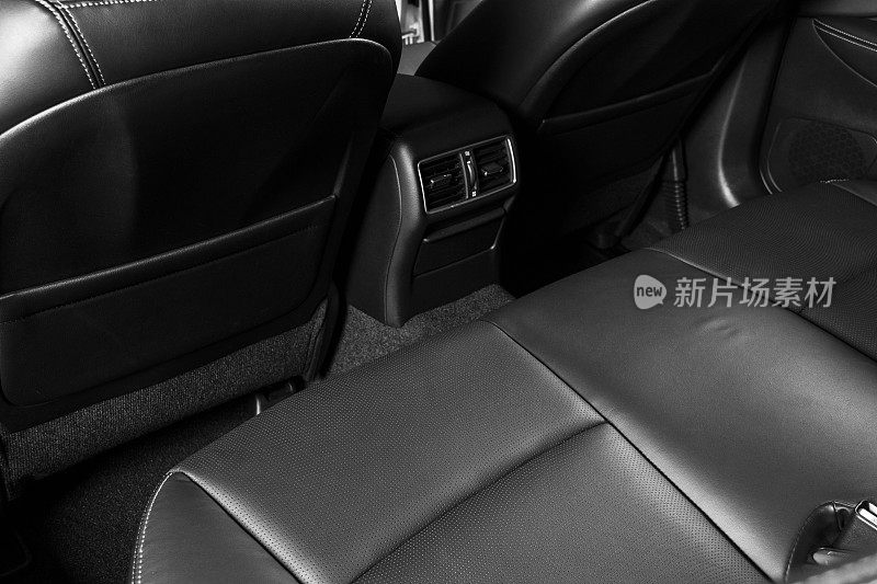 后排乘客座位，正面视图。黑色穿孔皮革与白色缝线。汽车详细。真皮舒适的黑色座椅。汽车内饰的细节