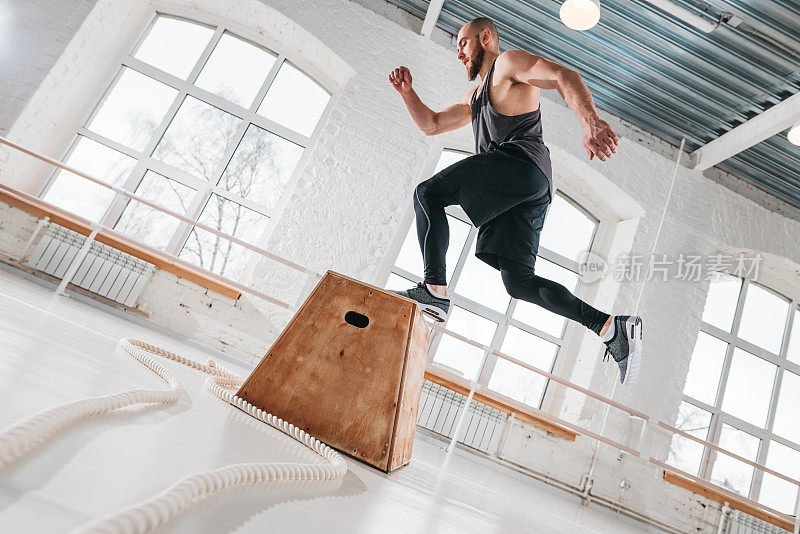 大胡子男运动员在体育馆里跳木箱，健身男在健身馆里做跳高运动，强身健腿