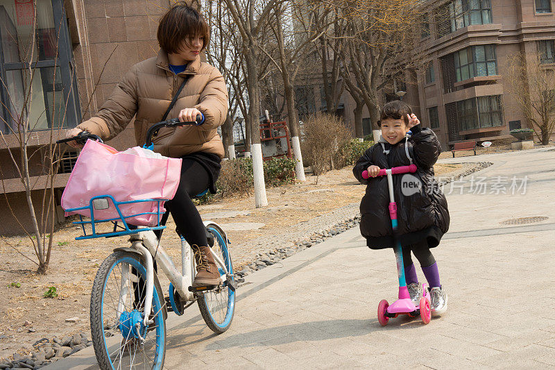 一个小女孩骑着滑板车跟在她妈妈后面