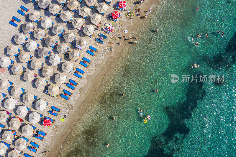 绿色的海岸线海滩，一个繁忙的海滩，充满了雨伞，日光浴床和人，从无人机上方拍摄