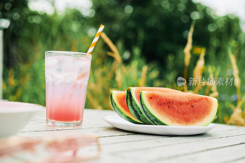 在一个炎热的夏天，花园的桌子上放着几片西瓜和一杯冰冻的粉色柠檬水。