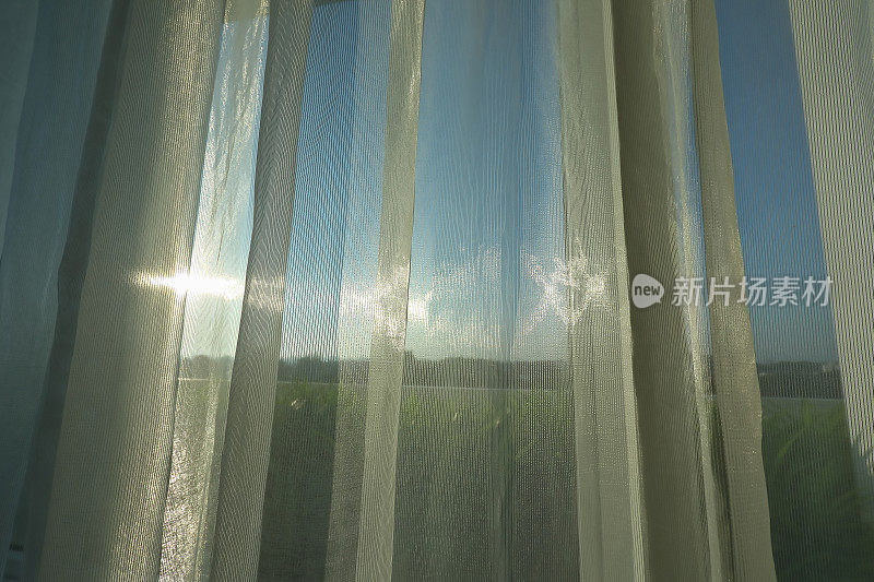 阳光透过白色的窗帘照射在窗户上