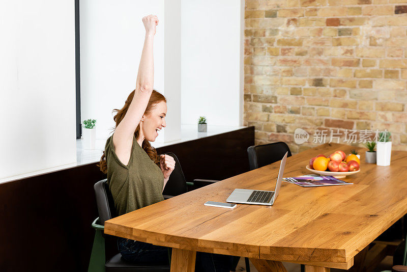 在家里桌子上的笔记本电脑和智能手机附近，快乐的女人显示耶手势的侧视图